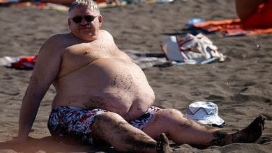 איש שמן סובל מהשמנת יתר יושב על חוף הים