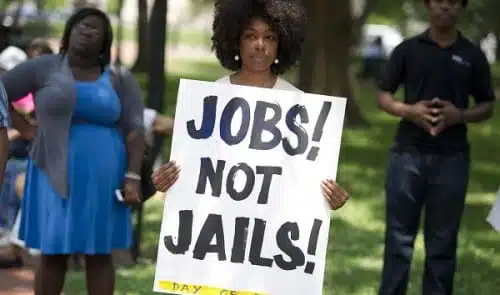 אישה מחזיקה שלט "תנו לנו עבודות, לא כלא"
