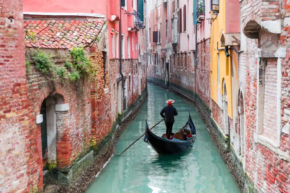 גונדולייר ונציאני מכוון גונדולה דרך מי התעלה הירוקים של ונציה, איטליה
